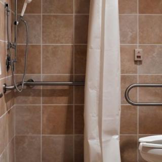 A tiled bathroom with a shower, curtain, and accessibility grab bars.