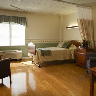 A well-lit hospital room with a bed, chairs, and a window.
