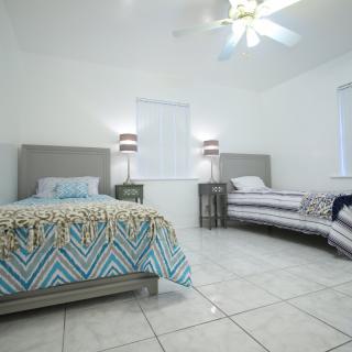 A bright, tiled bedroom featuring two beds with a ceiling fan and modern nightstands.