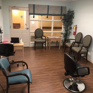 An empty waiting room with chairs and a small table, featuring a wooden floor and indoor plant.