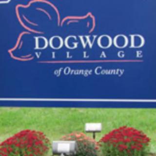 Sign for Dogwood Village of Orange County with red flowers in the foreground.
