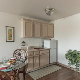 A small kitchen area with beige cabinets, a white refrigerator, and a dining table set for two.