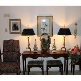 A well-decorated living room corner with a table, lamps, artwork, and chairs.