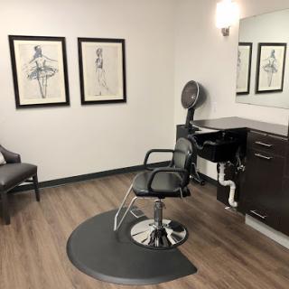 A minimalist hair salon featuring a stylist chair, mirror, and decorative artwork on the walls.