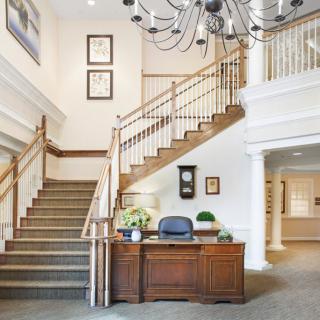 A well-lit interior space featuring a staircase and reception desk with a chandelier overhead.