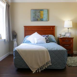 A cozy bedroom with a neatly made bed, a lamp on the nightstand, and a window allowing natural light in.