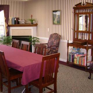 A cozy dining room with a table, chairs, and a bookshelf beside a decorated fireplace.