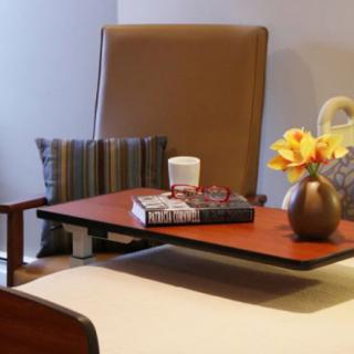 A cozy seating area with a comfortable chair, small table with books, a decorative vase with flowers, and a cushion.