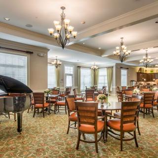 A spacious and elegantly decorated dining area featuring multiple tables, chairs, chandeliers, and a grand piano.