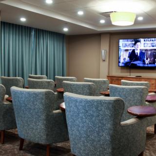 A small conference room with rows of comfortable chairs facing a television screen.