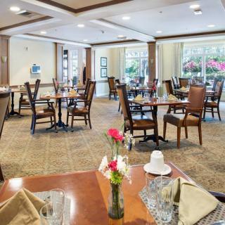A well-lit dining room with neatly arranged tables and chairs, decorated with flowers.