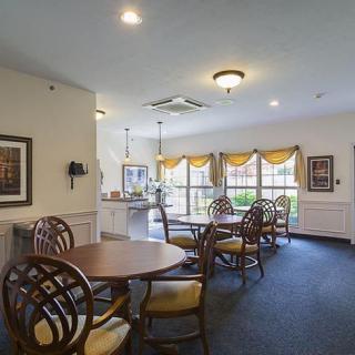 A cozy dining area with several round tables and chairs, adorned with warm lighting and large windows.