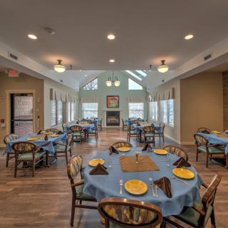 A well-lit dining room with multiple tables set for a meal, featuring large windows and elegant decor.