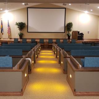 An empty auditorium with rows of cushioned seating facing a large projector screen in the front.