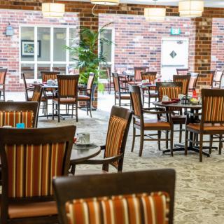 An empty restaurant dining area featuring wooden tables and chairs against a brick wall backdrop.