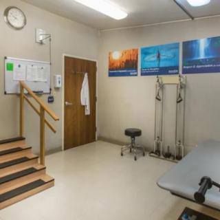 A physical therapy room equipped with exercise steps, a therapy table, and medical equipment, featuring colorful posters on the wall.