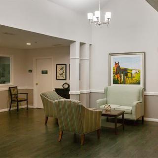 A cozy waiting area with a sofa and chairs arranged around a small table, illuminated by overhead lighting and adorned with wall paintings.