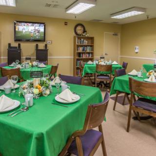 A neatly arranged dining room with green tablecloths and tables set for a meal.