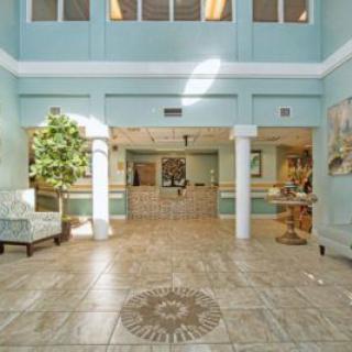 A spacious lobby with elegant tile flooring, featuring seating areas, columns, and a reception desk.