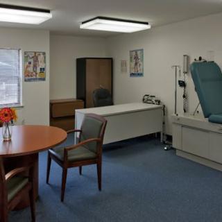 A clean and organized doctor's examination room with a bed, chairs, table, and medical equipment.