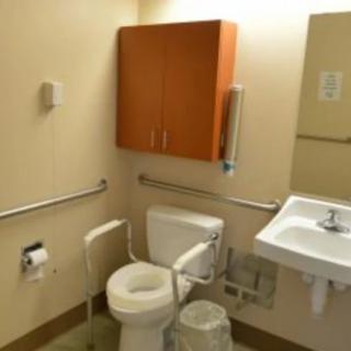 An accessible bathroom with a toilet, handrails, sink, and wooden cabinet.