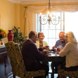 A group of seniors playing cards around a dining table in a well-lit room.