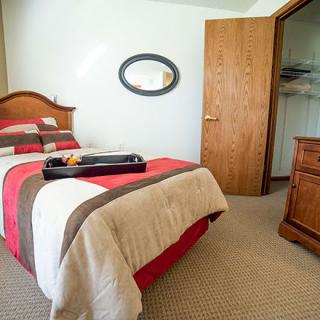 A cozy bedroom features a single bed with a striped duvet, wooden furniture, and an open closet door.