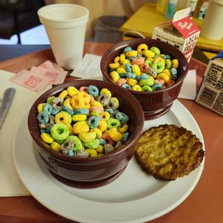 A vibrant breakfast featuring colorful cereal in bowls, accompanied by a cookie and a cup of milk.
