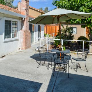 A sunny patio with a table and chairs set under an umbrella, surrounded by greenery.