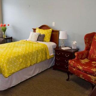 Single bedroom with a yellow bedspread, red armchair, and wooden nightstand.