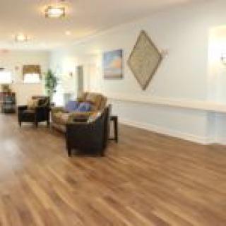 A spacious living room with wood flooring, featuring a sofa and chairs, decorated with artwork and plants.