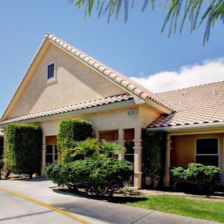 A sunny exterior view of a house with a sloped roof, surrounded by lush greenery.