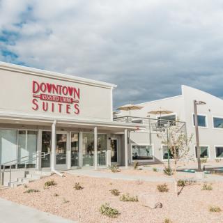 A modern hotel building with a 'Downtown Suites' sign against a cloudy sky, surrounded by desert landscaping.
