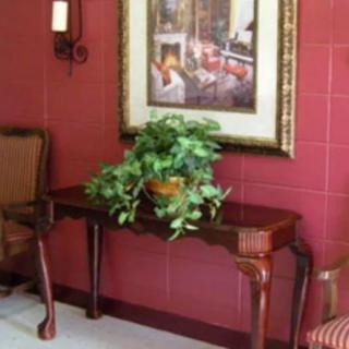 A cozy interior setting featuring a wooden console table with a potted plant, flanked by chairs and adorned with a framed painting on a red wall.