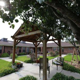 A serene outdoor courtyard featuring a wooden gazebo surrounded by lush greenery and seating.