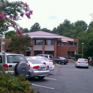 A parking lot in front of a brick office building, surrounded by trees and flowers.