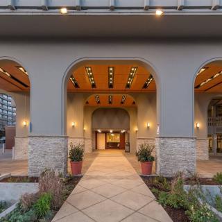 An elegant building entrance featuring multiple arches, illuminated by warm lighting, with potted plants and well-kept landscaping.