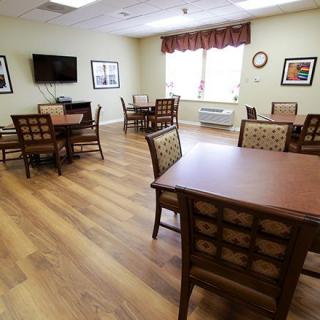 A cozy dining area with several tables and chairs, featuring a television and natural lighting.
