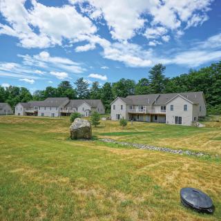 A row of houses in a suburban area with a large grassy field under a blue sky with clouds.