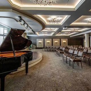 An elegant concert hall with a grand piano on stage and rows of empty chairs.