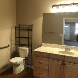 A bathroom with a toilet, sink, mirror, and storage shelf.