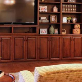 A cozy living room featuring an entertainment center with a large television and wooden bookshelves filled with decorative items.