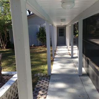 A covered outdoor walkway with white columns and a concrete path leading to the backyard.