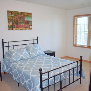 A tidy bedroom featuring a metal bed frame with patterned bedding, a painting on the wall, and a window bringing in natural light.