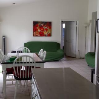 A cozy living room with a dining area featuring green sofas, a dining table with chairs, and wall art.