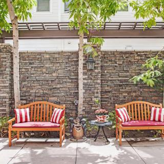 A cozy outdoor patio with wooden benches, striped pillows, and a small table set against a brick wall.