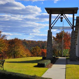 A scenic view of a bell tower with autumn foliage and a bench under a partly cloudy sky.