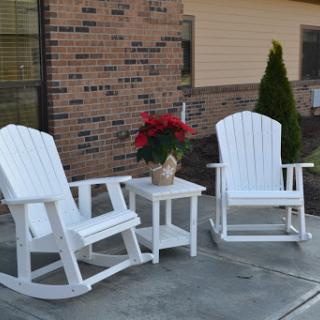 A serene outdoor seating area featuring two white rocking chairs and a potted plant.