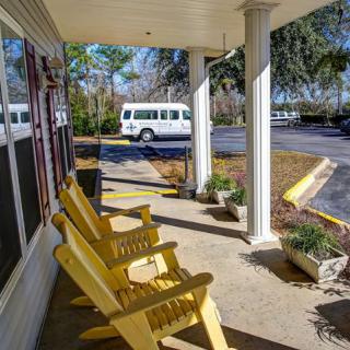 A sunny porch with yellow chairs overlooking a parking lot and a white van.