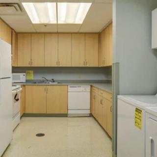 A modern kitchen with wooden cabinets and appliances including a refrigerator, microwave, dishwasher, and a nearby laundry area.